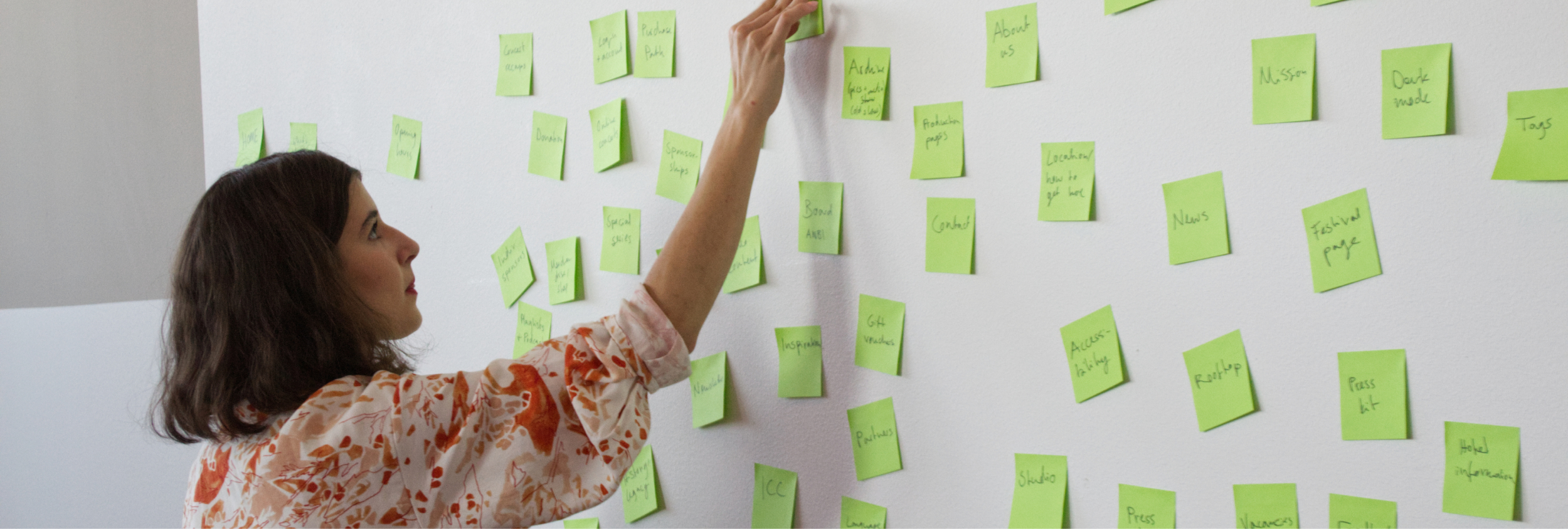 Julia is attaching a green post it note to a wall